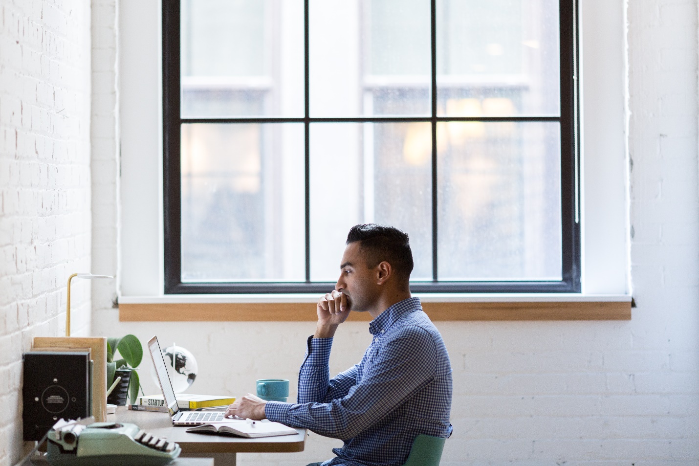 A man in a collared shirt sits at his desk by a window