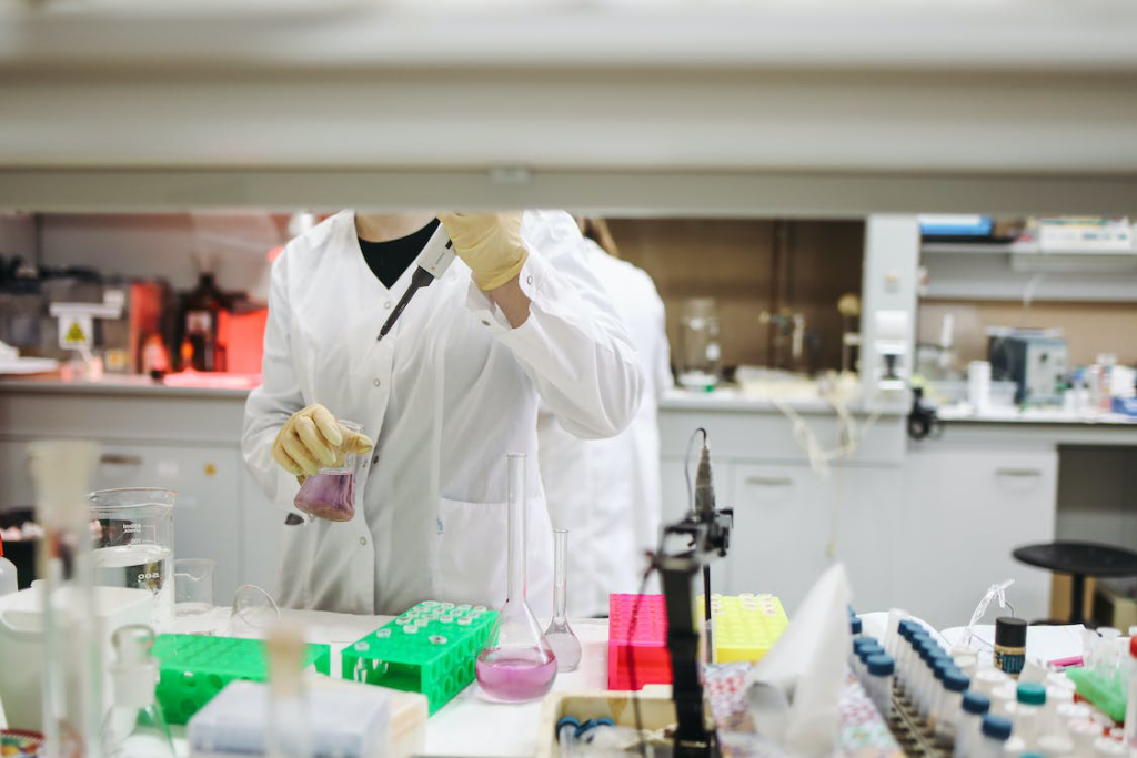 An image of a student wearing a lab coat and safety gloves working with chemicals in a university lab