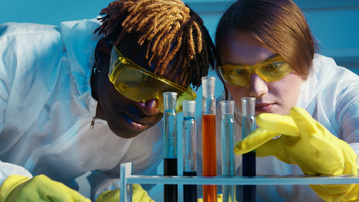An image of two students working with chemicals in a university lab wearing safety gloves and goggles
