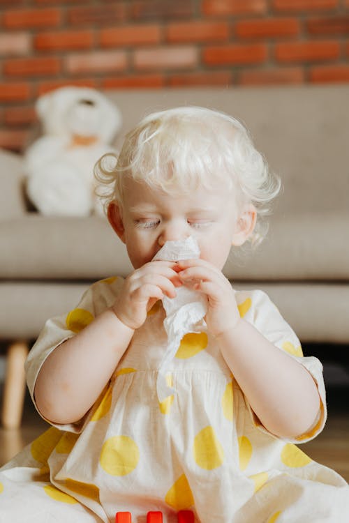 A baby girl rubbing her nose with a tissue, indicating symptoms of allergies.