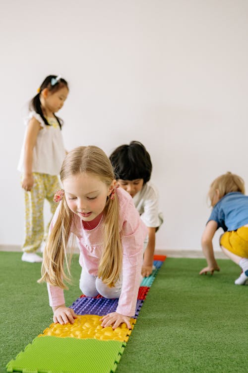 Children playing with colorful mats on a carpeted floor in a school.