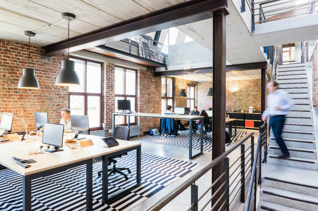 an office space with people working on desks and a person on stairs