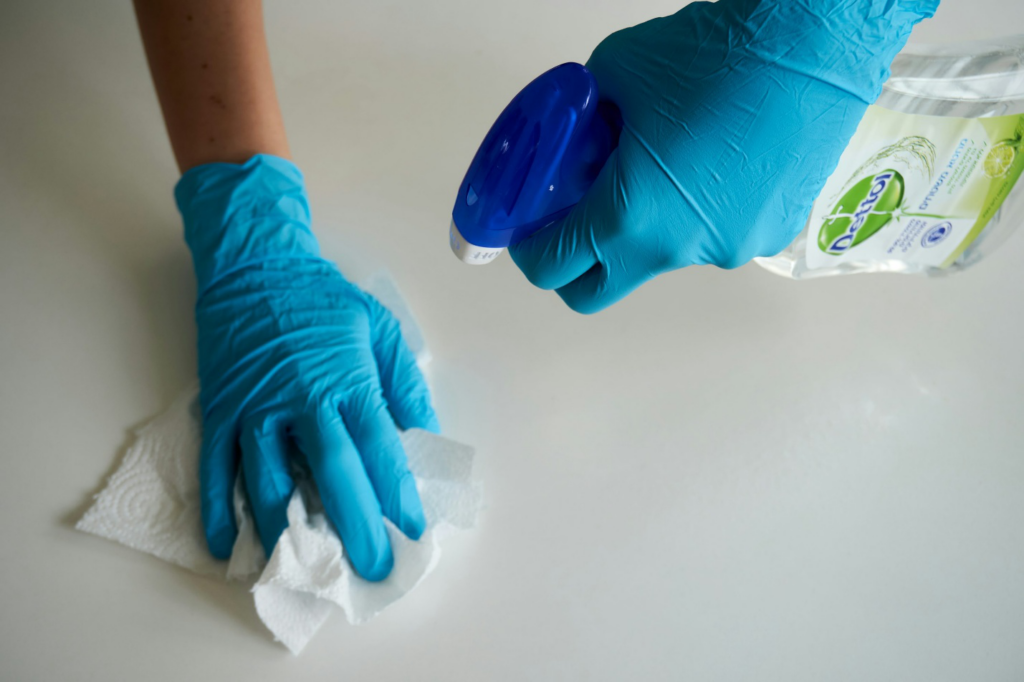 A person cleaning a white surface using Dettol spray