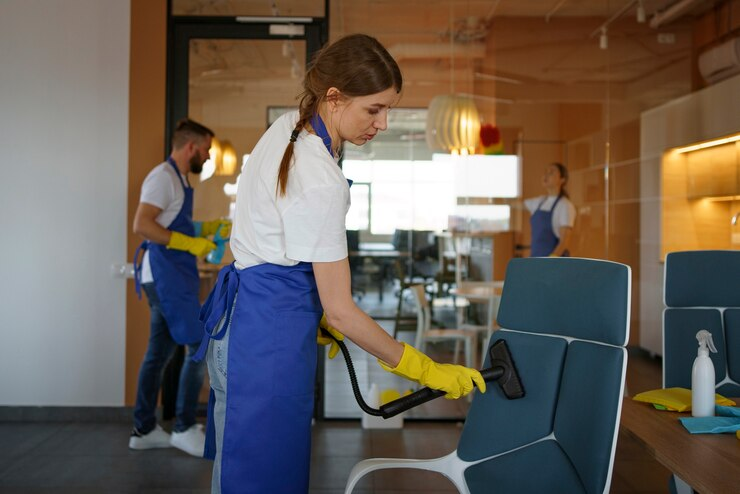 Woman using a vacuum cleaner to clean an office chair, demonstrating attention to detail in office cleaning.