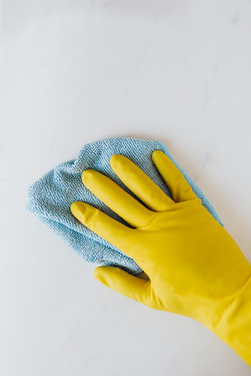 An image of a person wearing yellow gloves and wiping a surface with a blue towel