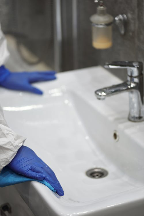 An image of a person wearing blue gloves while cleaning a sink