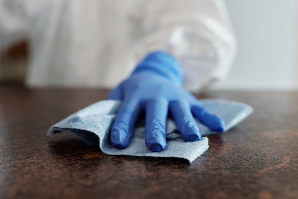 An image of a person wearing blue gloves and wiping a surface with a blue towel