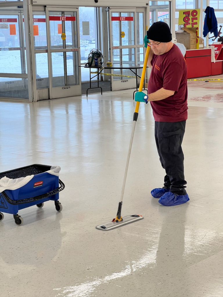 A janitor in uniform mops a shiny tile floor inside a brightly lit store