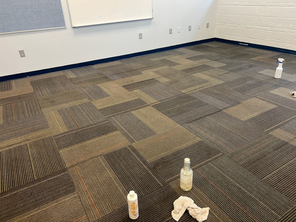 A commercial carpeted floor in an office setting, with cleaning supplies and cloths placed across the floor.