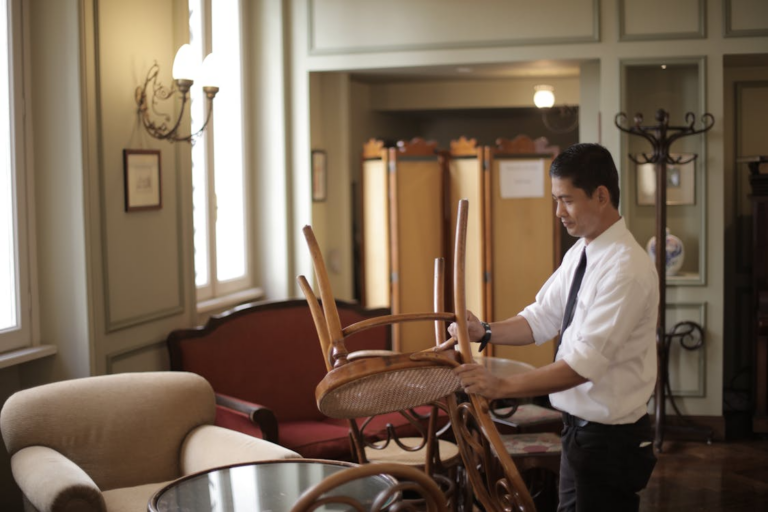 Restaurant dining area cleaning service in which the server is preparing tables and chairs before reopening